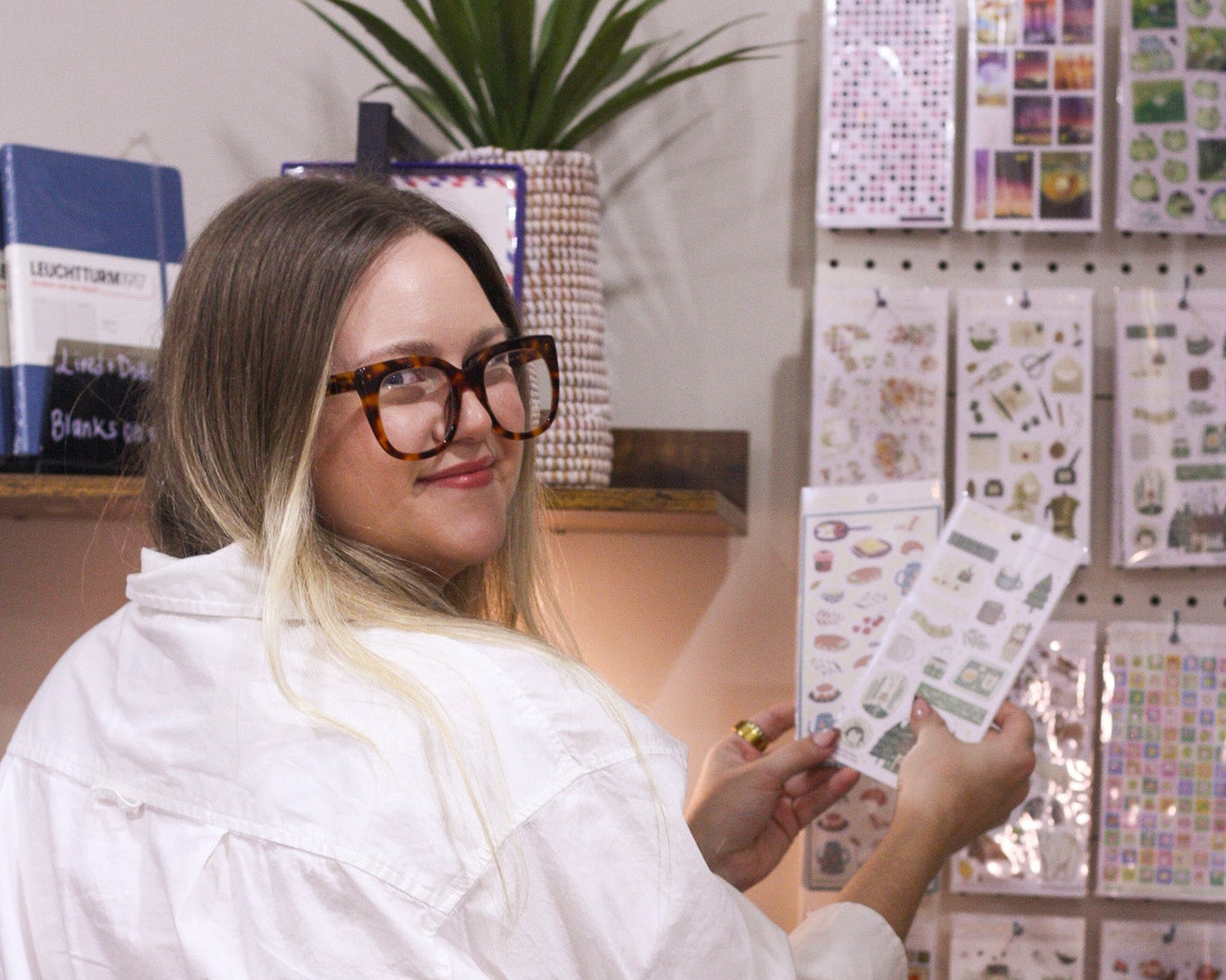 Woman in a white coat holding a sheet of stickers in front of a display of stickers.