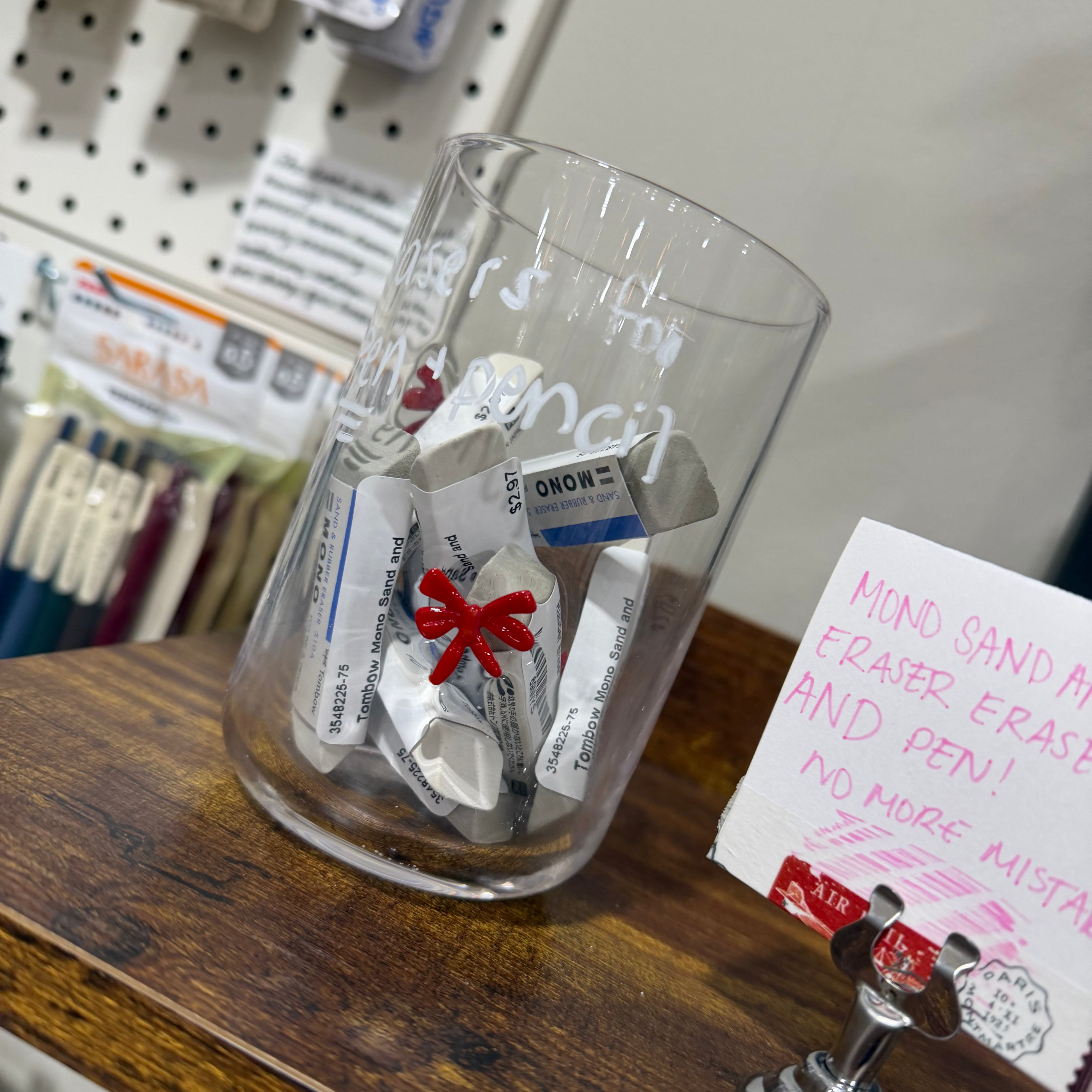 Glass container with erasers inside on wood shelf. 
