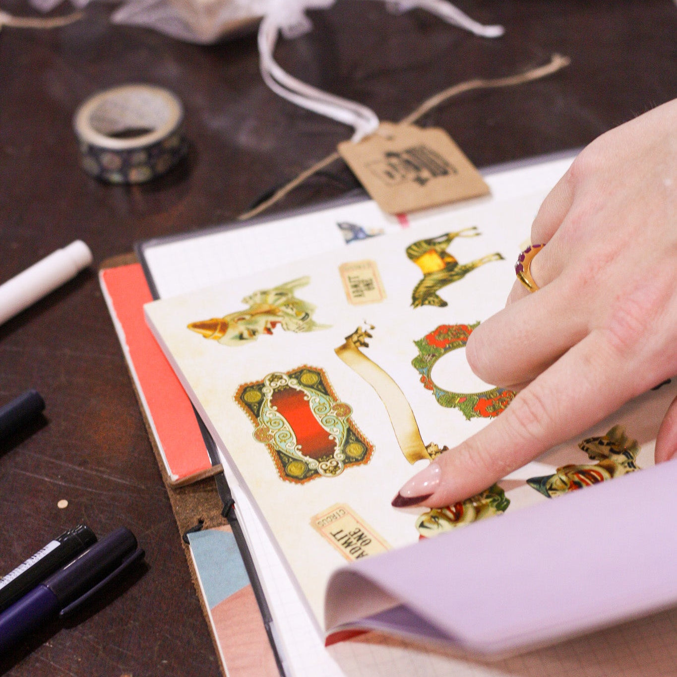 Hand holding a sheet of decorative stickers over an open notebook on a wooden surface.
